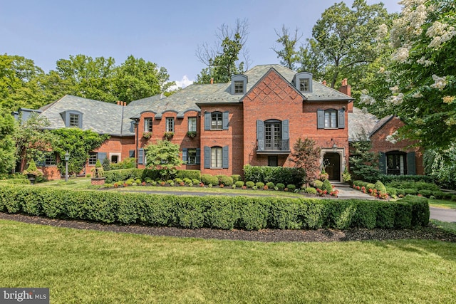 french country home with brick siding, a high end roof, and a front yard