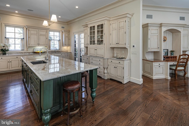 kitchen featuring a spacious island, glass insert cabinets, hanging light fixtures, light stone countertops, and a sink