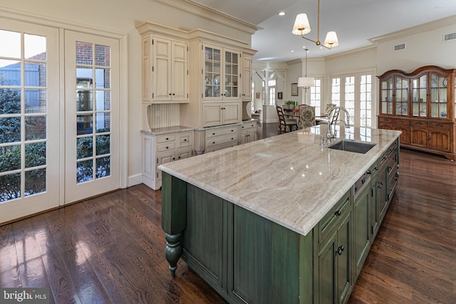 kitchen featuring glass insert cabinets, a sink, a center island with sink, decorative light fixtures, and green cabinetry