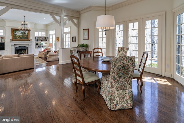 dining area with a notable chandelier, a fireplace, wood finished floors, baseboards, and crown molding