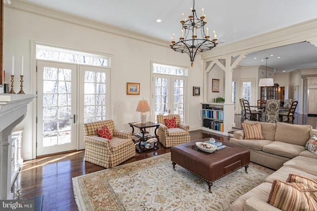 living area featuring french doors, a fireplace, a notable chandelier, ornamental molding, and wood finished floors