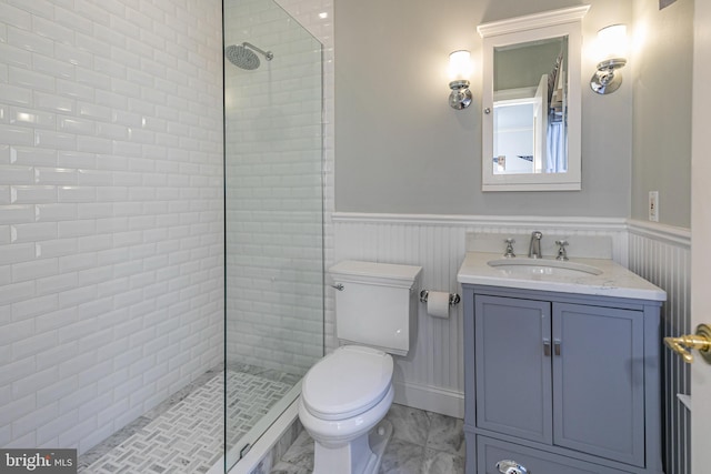 full bath featuring toilet, a wainscoted wall, vanity, marble finish floor, and tiled shower