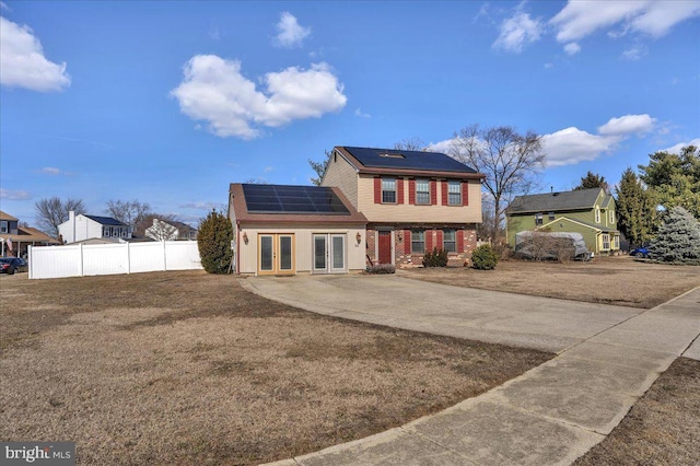 colonial inspired home featuring solar panels, french doors, a front yard, and fence