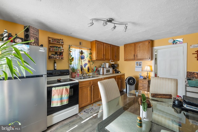 kitchen featuring electric range, white microwave, brown cabinetry, freestanding refrigerator, and a sink