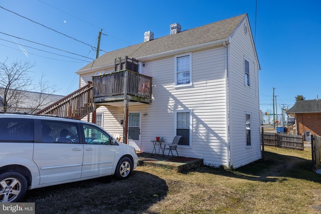rear view of house featuring a shingled roof, fence, a lawn, stairway, and a chimney