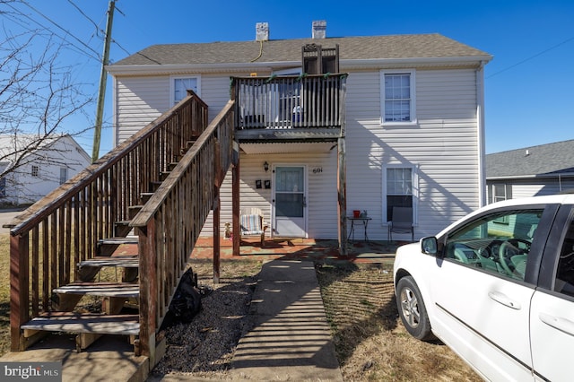 rear view of house with a shingled roof, a chimney, and stairway