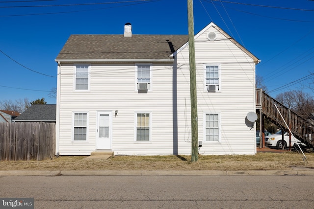 view of front of house with entry steps, a shingled roof, a chimney, and fence