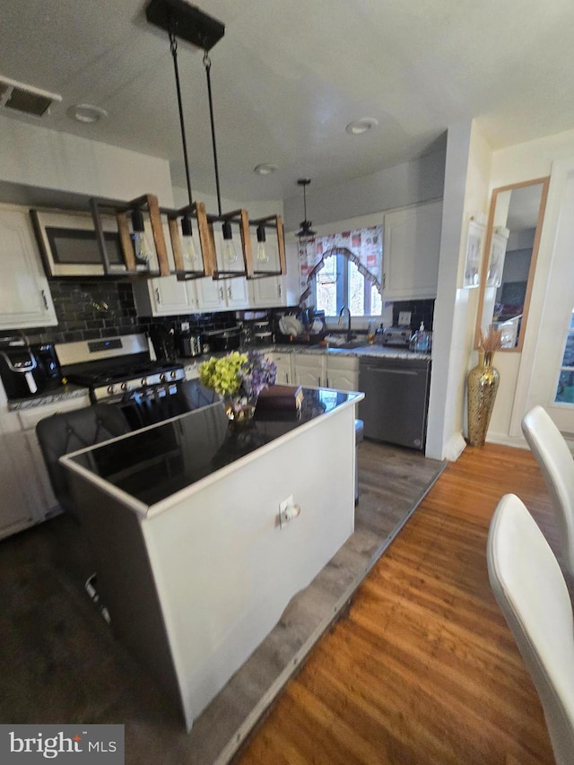 kitchen featuring tasteful backsplash, dark countertops, white cabinetry, a sink, and wood finished floors