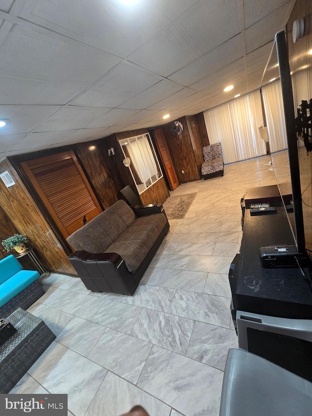 living room with visible vents, wooden walls, and a drop ceiling