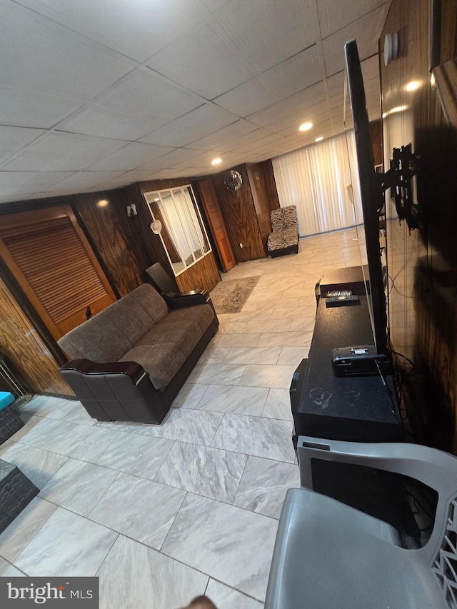 living area featuring a drop ceiling and wooden walls