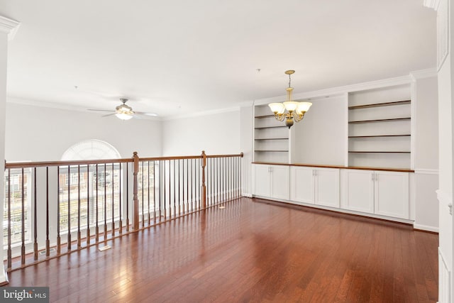 unfurnished room with ceiling fan with notable chandelier, wood-type flooring, built in features, and crown molding