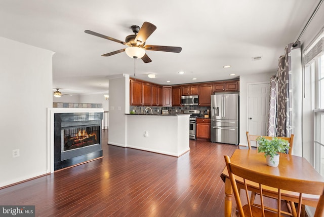 kitchen featuring tasteful backsplash, dark countertops, dark wood-style floors, a peninsula, and stainless steel appliances