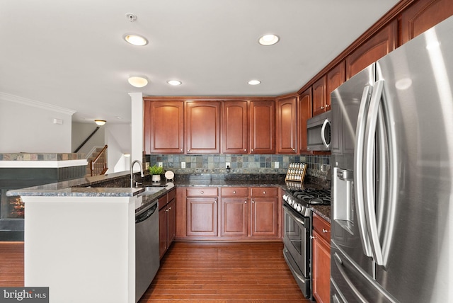 kitchen with stainless steel appliances, a peninsula, dark wood-style floors, tasteful backsplash, and dark stone countertops