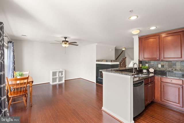 kitchen featuring dark wood finished floors, a glass covered fireplace, a sink, dishwasher, and a peninsula