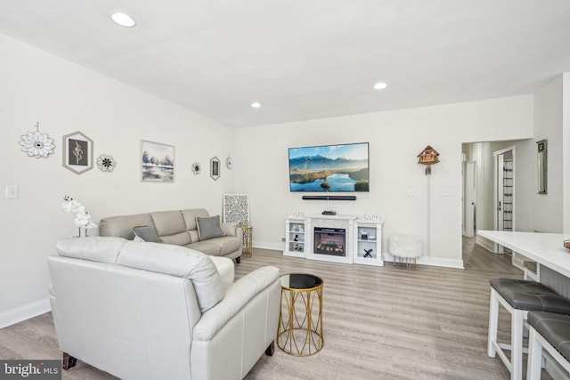 living room with baseboards, light wood finished floors, a glass covered fireplace, and recessed lighting