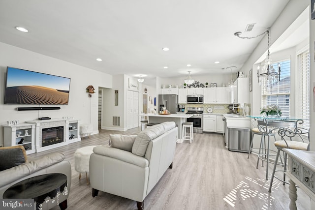 living room with recessed lighting, a glass covered fireplace, visible vents, and light wood-style floors