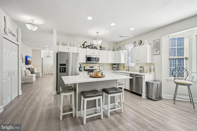 kitchen with light wood-style flooring, light countertops, appliances with stainless steel finishes, backsplash, and a kitchen bar