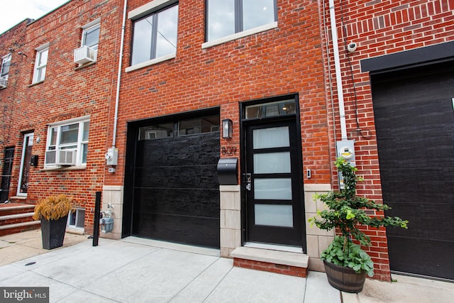 view of exterior entry with an attached garage, cooling unit, and brick siding