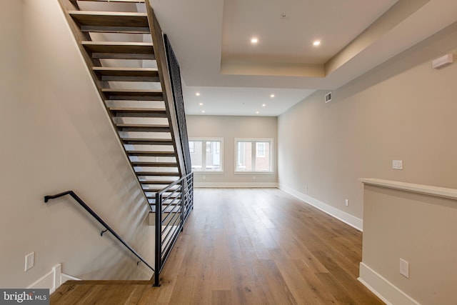 stairway with baseboards, a tray ceiling, hardwood / wood-style floors, and recessed lighting