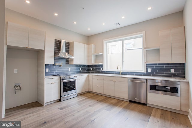 kitchen with stainless steel appliances, light countertops, wall chimney range hood, open shelves, and a sink