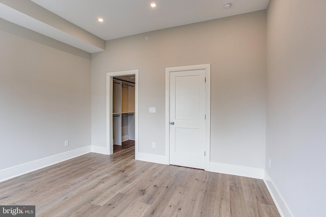 unfurnished bedroom featuring light wood-type flooring, baseboards, a walk in closet, and recessed lighting