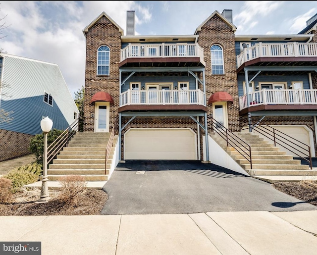 view of property with an attached garage, driveway, stairs, and brick siding