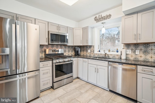 kitchen with appliances with stainless steel finishes, dark stone countertops, a sink, gray cabinetry, and backsplash