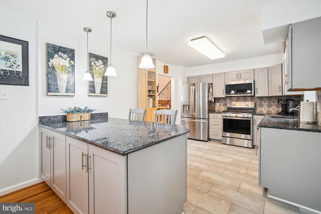 kitchen featuring tasteful backsplash, dark stone counters, appliances with stainless steel finishes, decorative light fixtures, and a peninsula