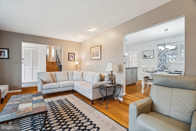 living area with stairs, light wood finished floors, a chandelier, and baseboards