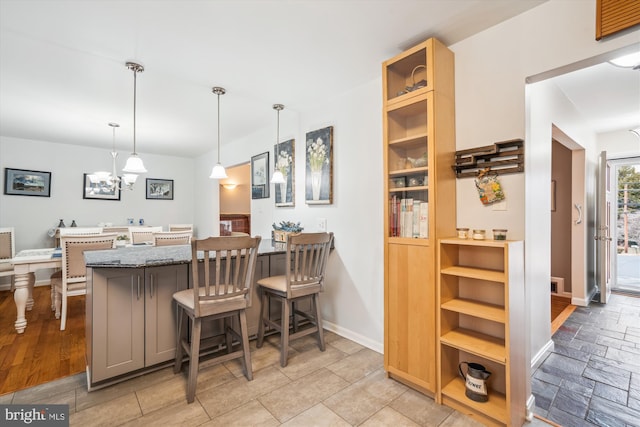 kitchen featuring baseboards, dark stone counters, a kitchen breakfast bar, decorative light fixtures, and a peninsula