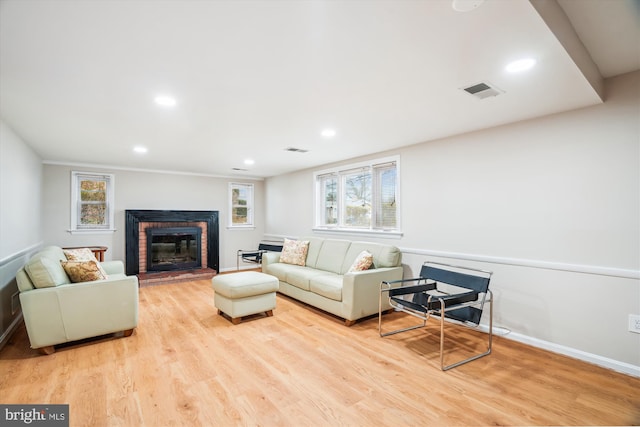 living room featuring visible vents, light wood finished floors, a brick fireplace, and a wealth of natural light