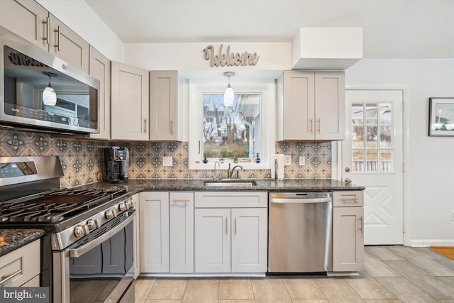 kitchen featuring a sink, baseboards, appliances with stainless steel finishes, tasteful backsplash, and dark stone countertops