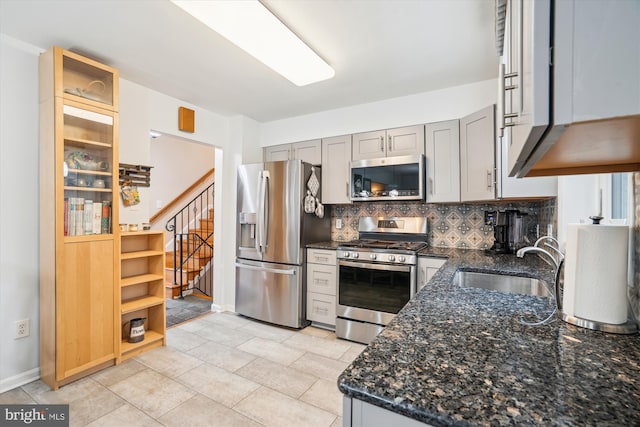 kitchen with decorative backsplash, appliances with stainless steel finishes, dark stone countertops, gray cabinets, and a sink