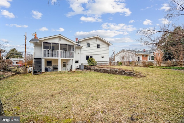 rear view of house featuring a sunroom, a chimney, fence, and a lawn