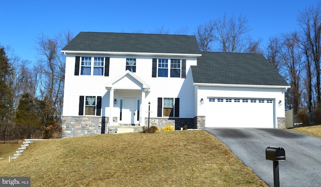 colonial home featuring a garage, stone siding, driveway, and a front lawn