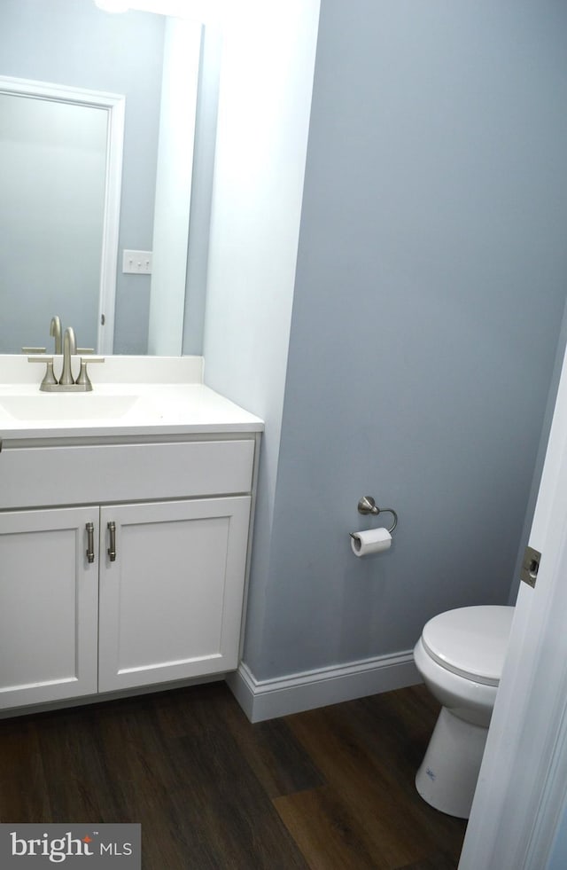 half bathroom featuring baseboards, vanity, toilet, and wood finished floors