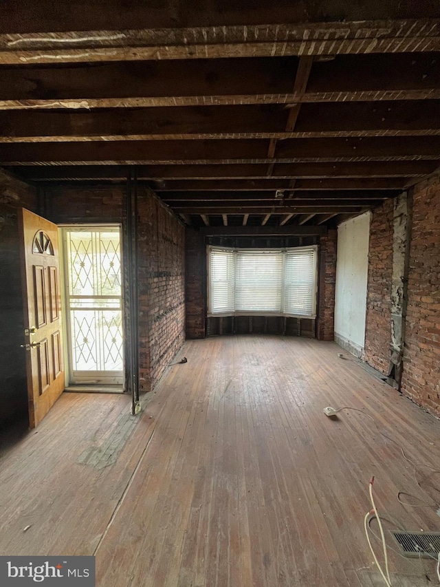 interior space featuring brick wall, beam ceiling, and wood finished floors