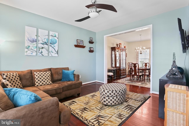 living area with ceiling fan with notable chandelier, hardwood / wood-style flooring, and baseboards