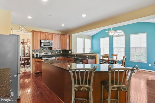 kitchen with a sink, appliances with stainless steel finishes, a center island, dark wood-style floors, and tasteful backsplash