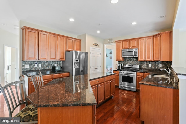 kitchen with a center island, dark wood finished floors, stainless steel appliances, a sink, and dark stone countertops