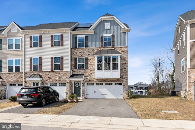 multi unit property featuring driveway, stone siding, a garage, and board and batten siding