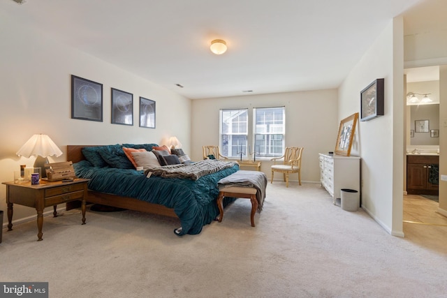 bedroom featuring visible vents, light carpet, ensuite bathroom, a sink, and baseboards