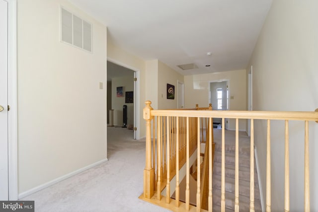 hallway featuring an upstairs landing, visible vents, baseboards, and carpet floors