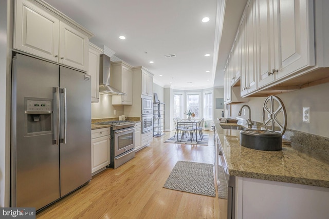 kitchen featuring recessed lighting, a sink, appliances with stainless steel finishes, wall chimney range hood, and light wood finished floors