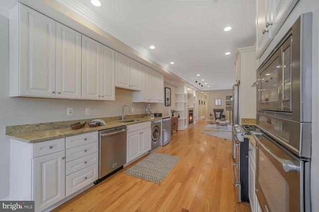 kitchen with appliances with stainless steel finishes, ornamental molding, white cabinets, a sink, and washer / dryer