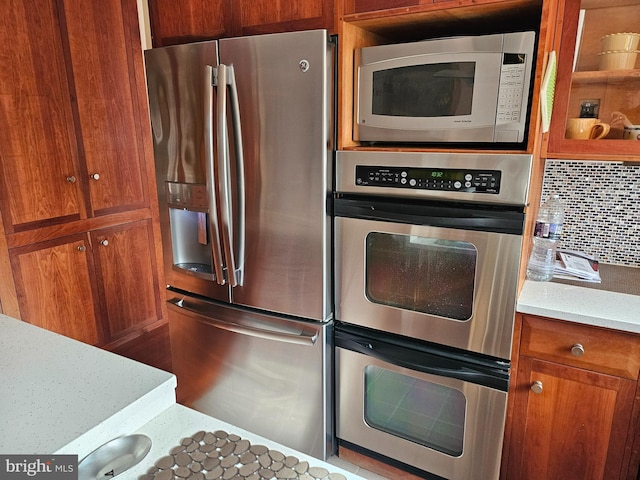 kitchen featuring light stone counters, backsplash, brown cabinetry, and appliances with stainless steel finishes