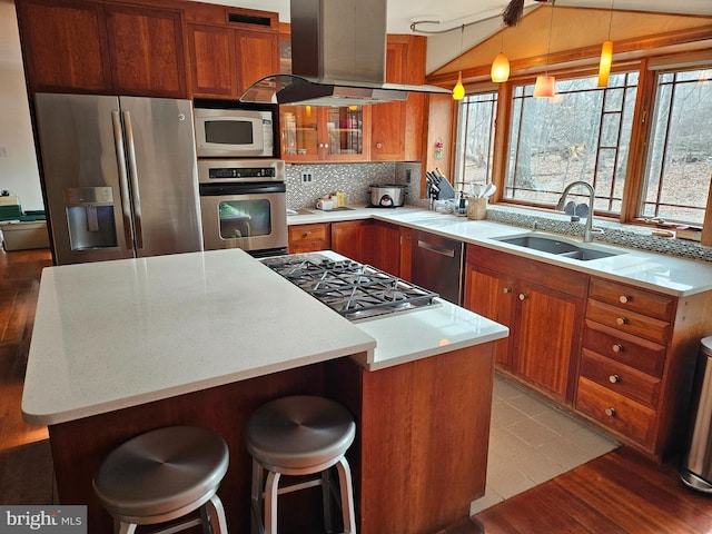 kitchen featuring a sink, appliances with stainless steel finishes, wall chimney exhaust hood, brown cabinetry, and vaulted ceiling