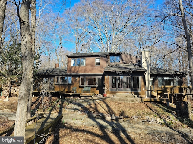 back of house featuring roof with shingles and a chimney