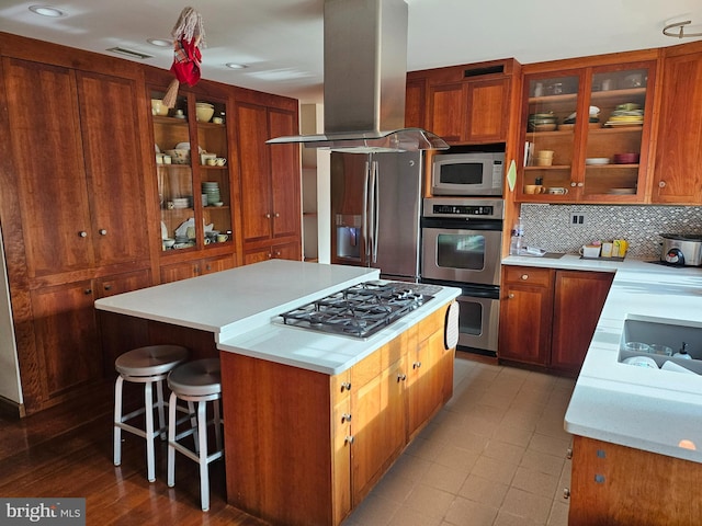 kitchen with backsplash, a kitchen island, island exhaust hood, brown cabinetry, and stainless steel appliances