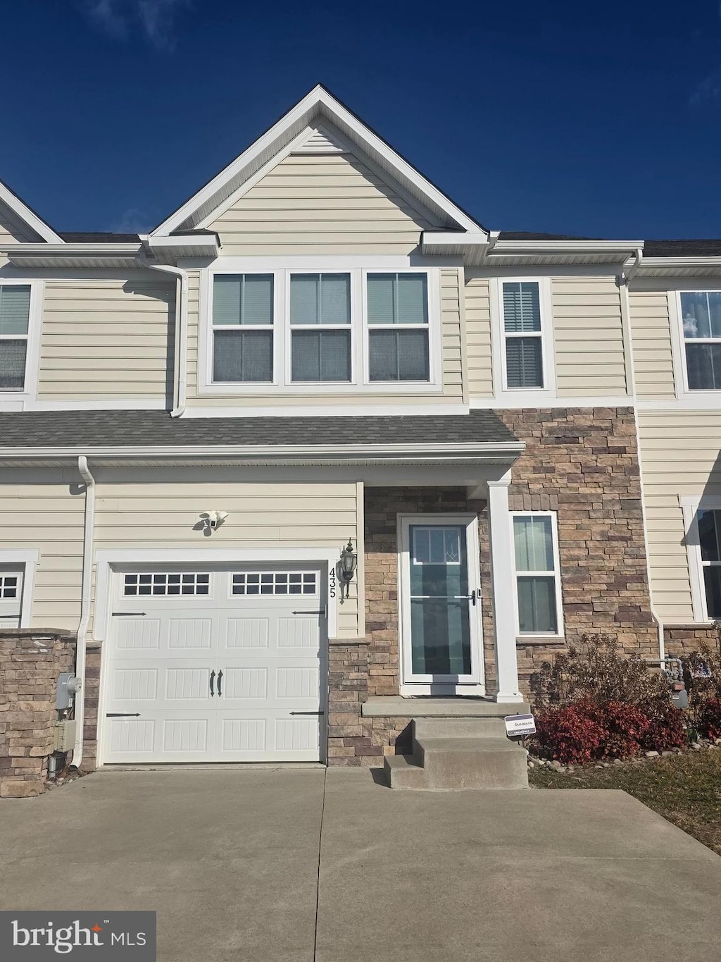 townhome / multi-family property with stone siding, an attached garage, and driveway